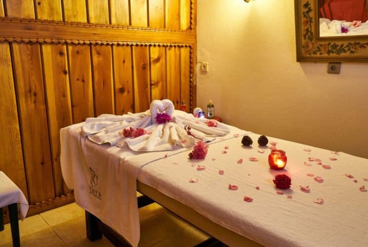 Spa room with table covered with white towels, flower petals and a lit candle