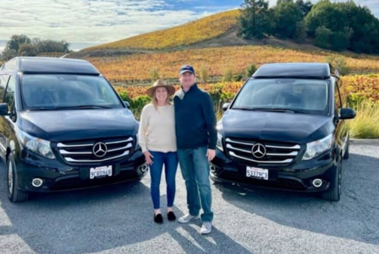 A man and woman standing outside with two Mercedes vans in a parking lot