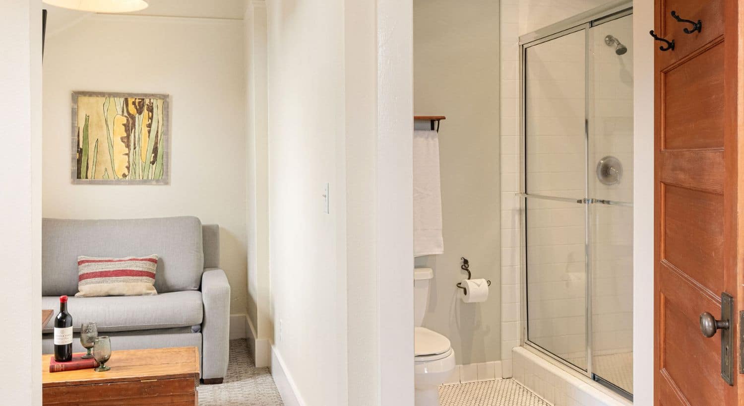 View of a room with sitting room on one side of a wall and bathroom with toilet and glass-door shower on the other side