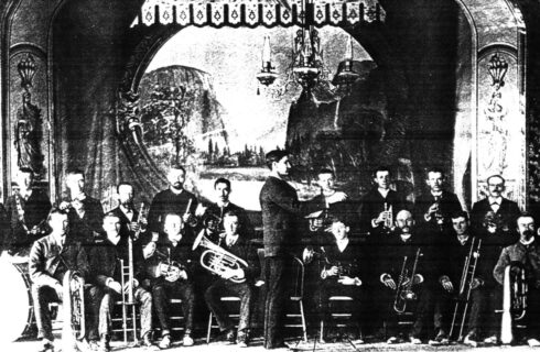 Historic black and white photograph of a group of men sitting in chairs, each holding an instrument