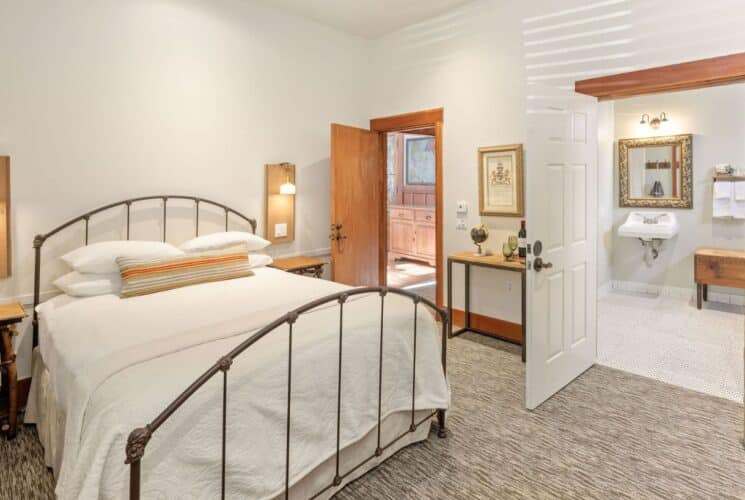 Bedroom suite with bed with curved headboard and footboard, side tables, sitting chair and door open to a large bathroom