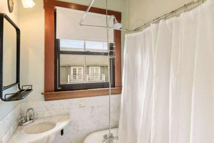 Bathroom with clawfoot tub, white shower curtain, corner sink with mirror, window with a white shade