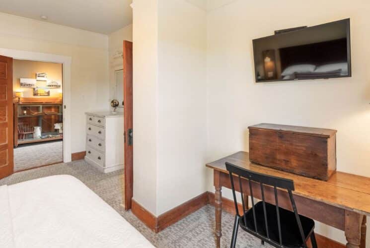 Bedroom with bed, desk with black chair TV, and doorway into a hallway