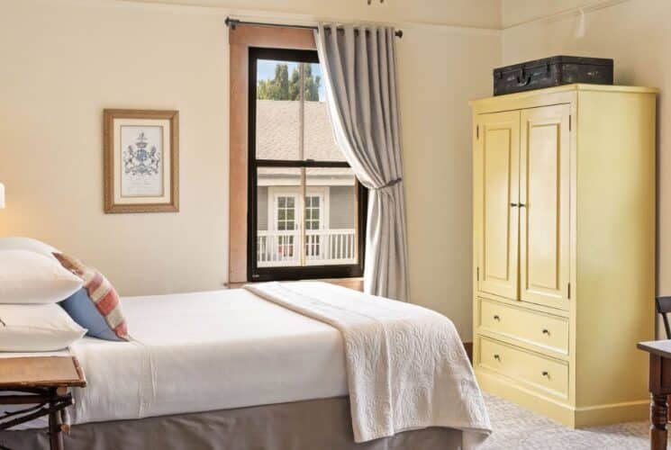 Cozy bedroom with bed, yellow armoire, large window with curtain pulled back