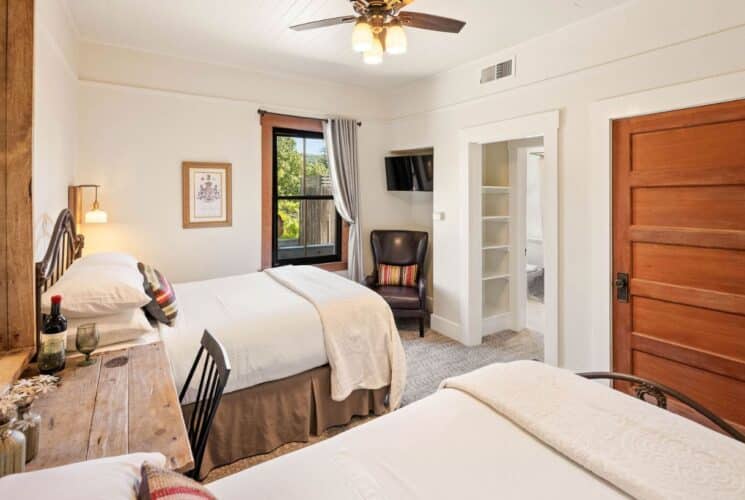 Spacious bedroom suite with two beds, wood desk and chair under a large mirror, doorway into a bathroom