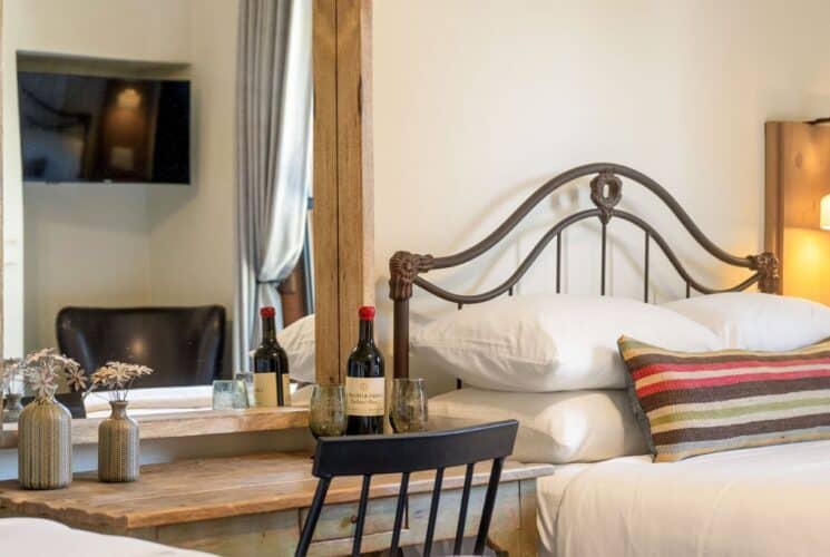 Bedroom with queen bed, wood desk with chair, bottle of wine and two glasses, large wood framed mirror