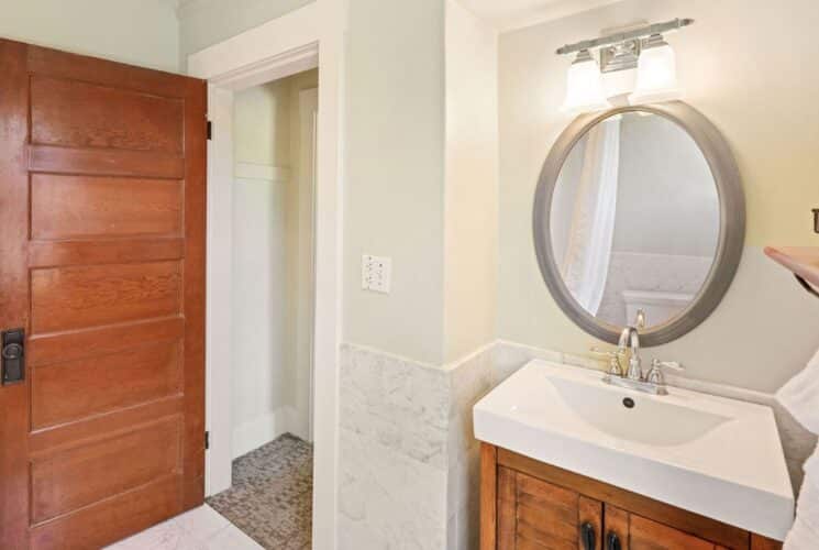 Bathroom with single sink, oval mirror, plush white towels hanging on a rack with a wood shelf, large wood door