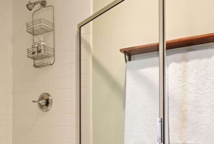 Bathroom with shower with glass doors, plush white towels hanging on a rack with a wood shelf