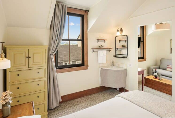 Spacious bedroom suite with bed, dresser, corner sink with mirror and towel rack, window and adjacent sitting room