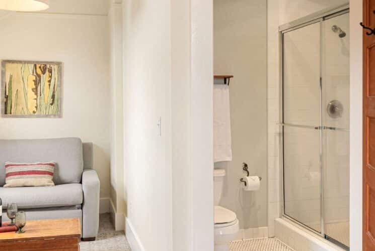 Sitting room with couch, table with wine and glasses, adjacent to a bathroom with glass-door shower