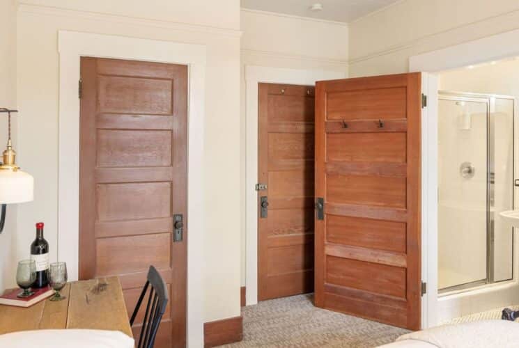 Bedroom with bed, desk with chair, door open to a bathroom with glass door shower and pedestal sink