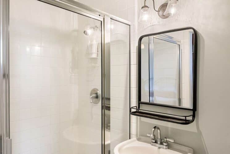 Bathroom with glass door shower, pedestal sink with black framed mirror