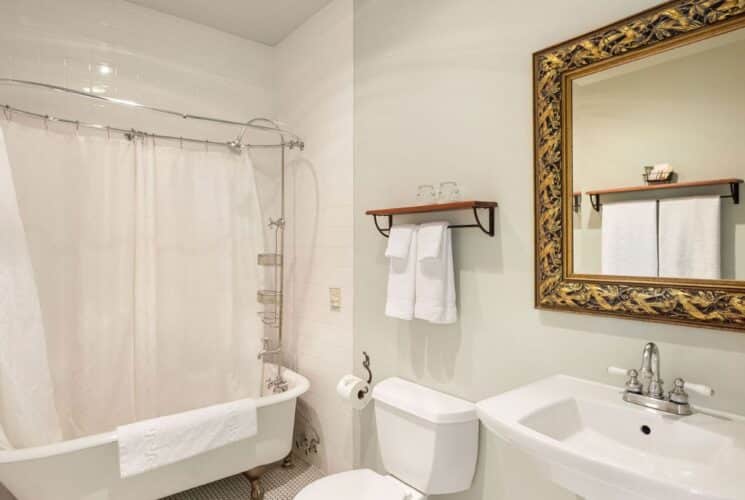 Bathroom with clawfoot tub, pedestal sink, gold framed mirror, white towels on a rack