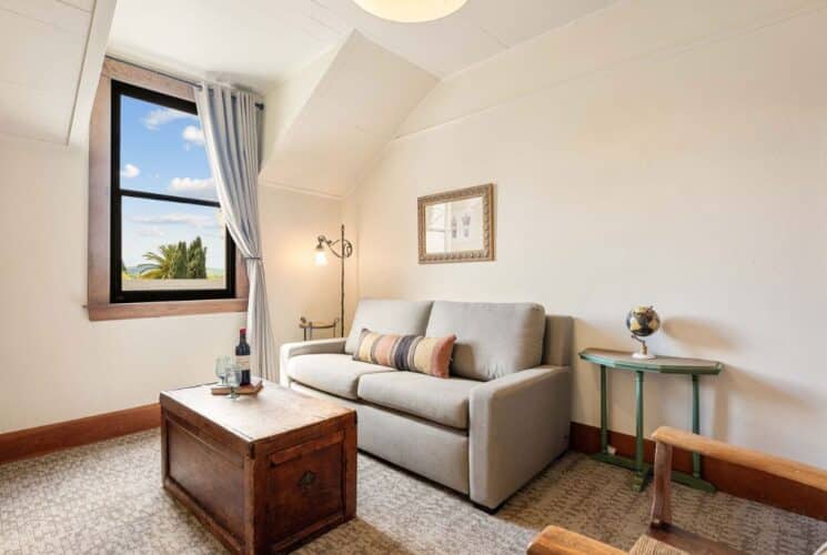 Sitting room with loveseat, chest, lamp, table with globe and large window with curtain pulled back