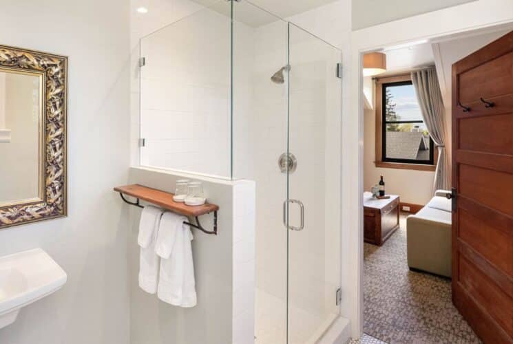 Bathroom with pedestal sink, large framed mirror, hanging towels, shower with glass doors and doorway open to a bedroom