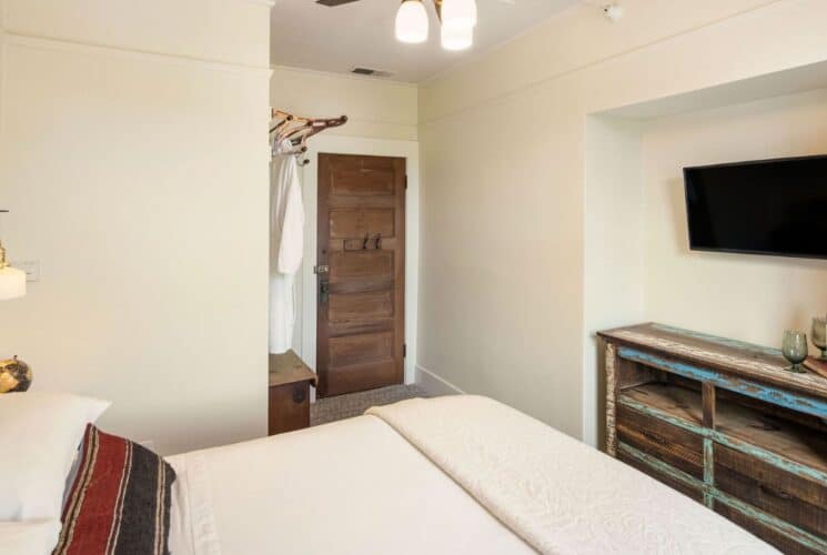 Bedroom with queen bed, dresser with TV in a nook, plush robes hanging on hooks by the door