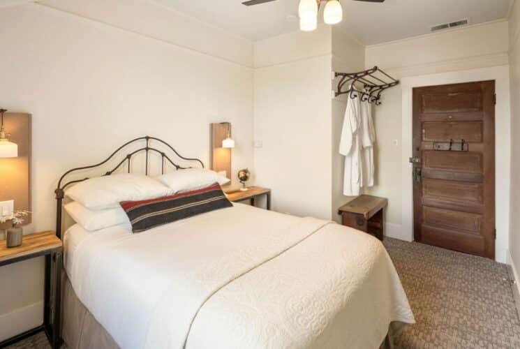 Bedroom with queen bed in white linens, side tables with lamps, plush robes hanging on hooks by a door