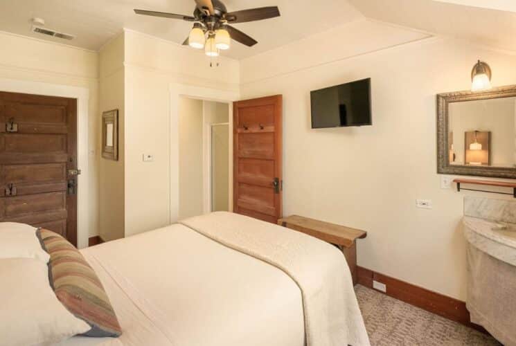 Cozy bedroom with queen bed in white, corner sink, mirror, TV and two wood doors