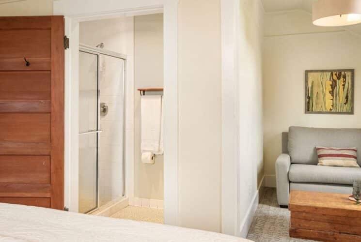 Bedroom suite with bed, adjacent sitting room with couch and table, doorway open to a bathroom with glass-door shower