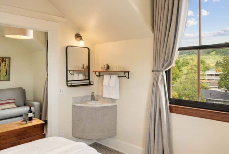 Bedroom suite with corner sink, mirror, wood shelf, doorway into sitting room with couch and table