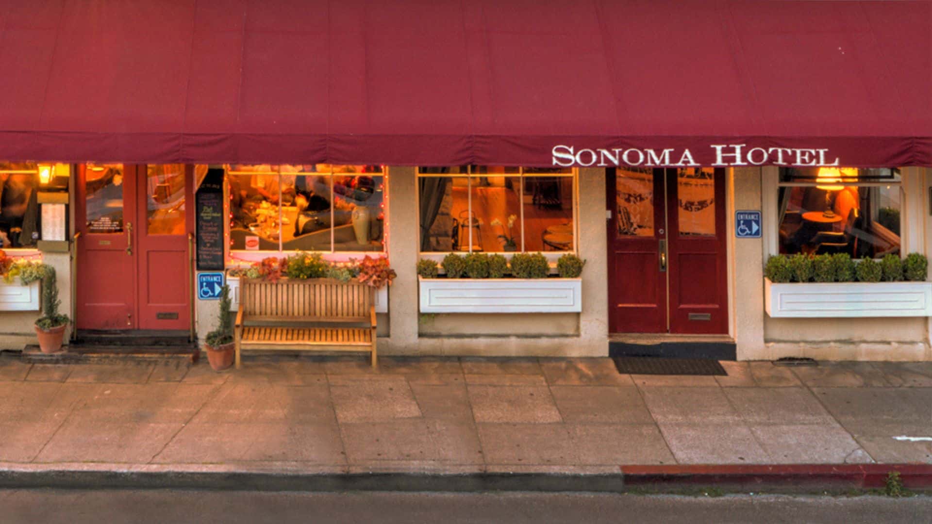 Front view of a hotel with a red canopy, window boxes and sidewalk out front