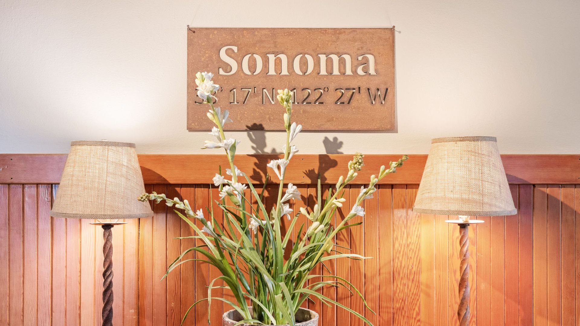 Metal sign for a hotel with coordinates engraved, two lamps and potted plant with white flowers