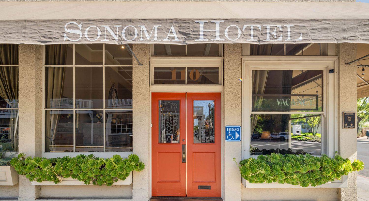 Front facade of a hotel with large windows, orange double door and canopy with hotel name